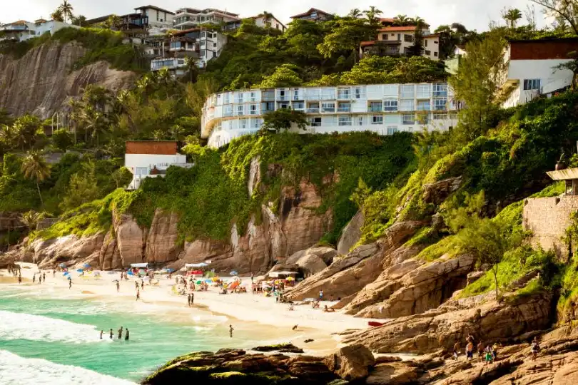 Praia charmosa do Rio de Janeiro com pessoas aproveitando o mar e a areia, com a comunidade local e a natureza exuberante em contraste.