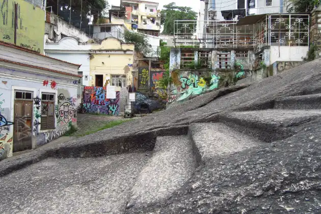 Formação rochosa da Pedra do Sal com marcas do tempo, cercada por construções modestas e arte urbana, representando a história e a cultura afro-brasileira no Rio.