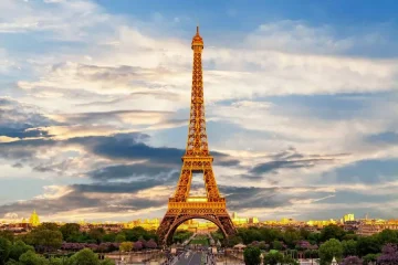 Vista da Torre Eiffel em Paris sob um céu com nuvens e a cidade ao fundo.