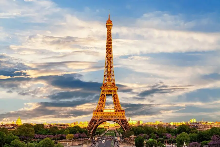Vista da Torre Eiffel em Paris sob um céu com nuvens e a cidade ao fundo.