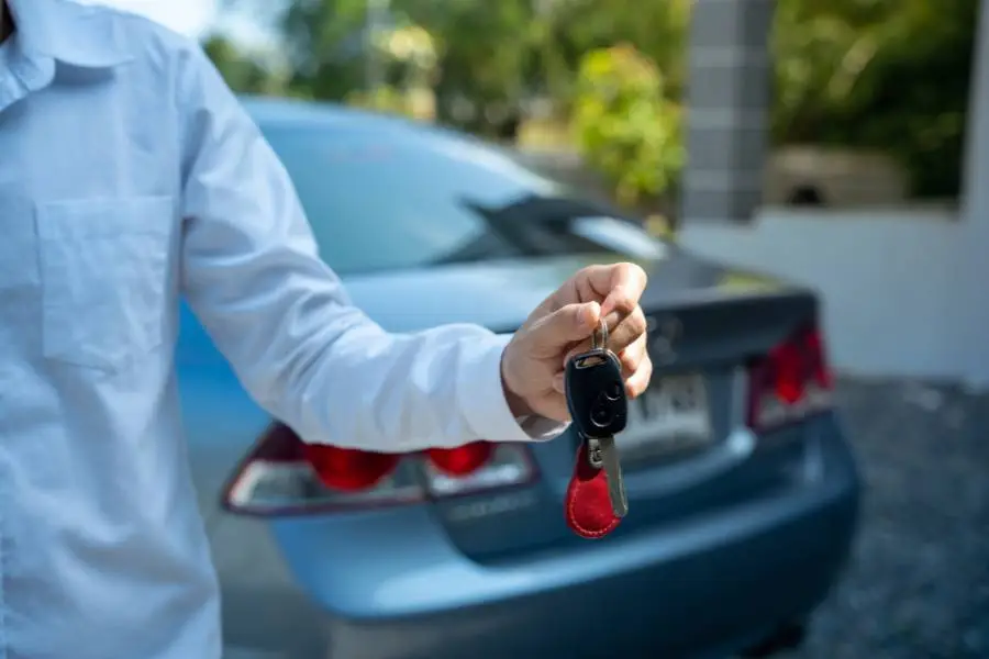 Pessoa segurando a chave de um carro prata, sugerindo a locação de um veículo