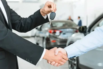 Aperto de mãos entre vendedor e locador de carro, com chave do veículo em destaque.