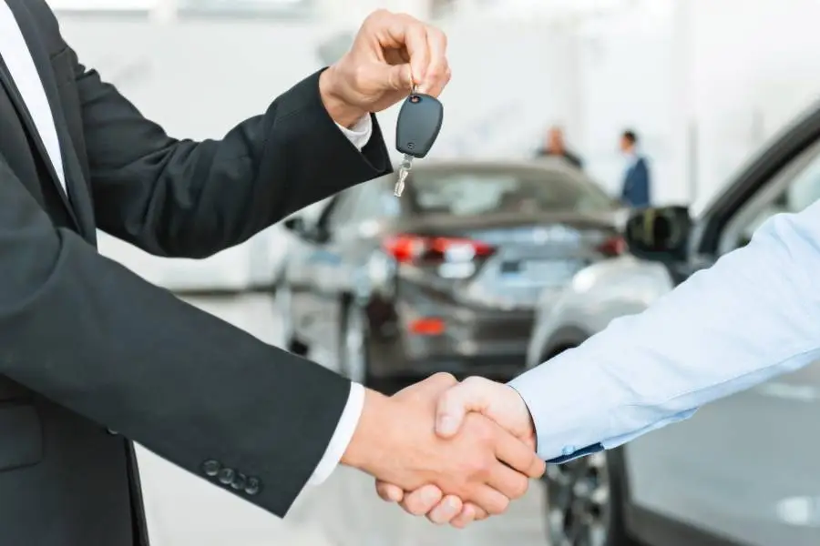 Aperto de mãos entre vendedor e locador de carro, com chave do veículo em destaque.