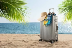 Mala de alumínio Rimowa na praia com acessórios de viagem como chapéu e óculos de sol.