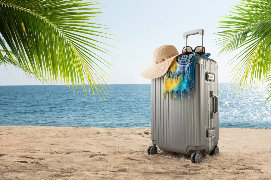 Mala de alumínio Rimowa na praia com acessórios de viagem como chapéu e óculos de sol.