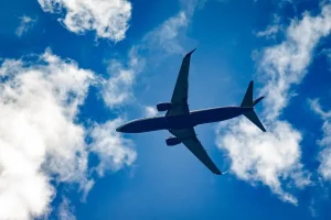 Avião comercial voando em céu azul com nuvens brancas visto de baixo.